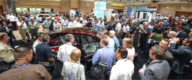 people gethered in a crowd in front of a red car in an exhibition stand